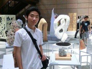 自らの作品展示の前で「作品＝石の模刻（木の台の上）」